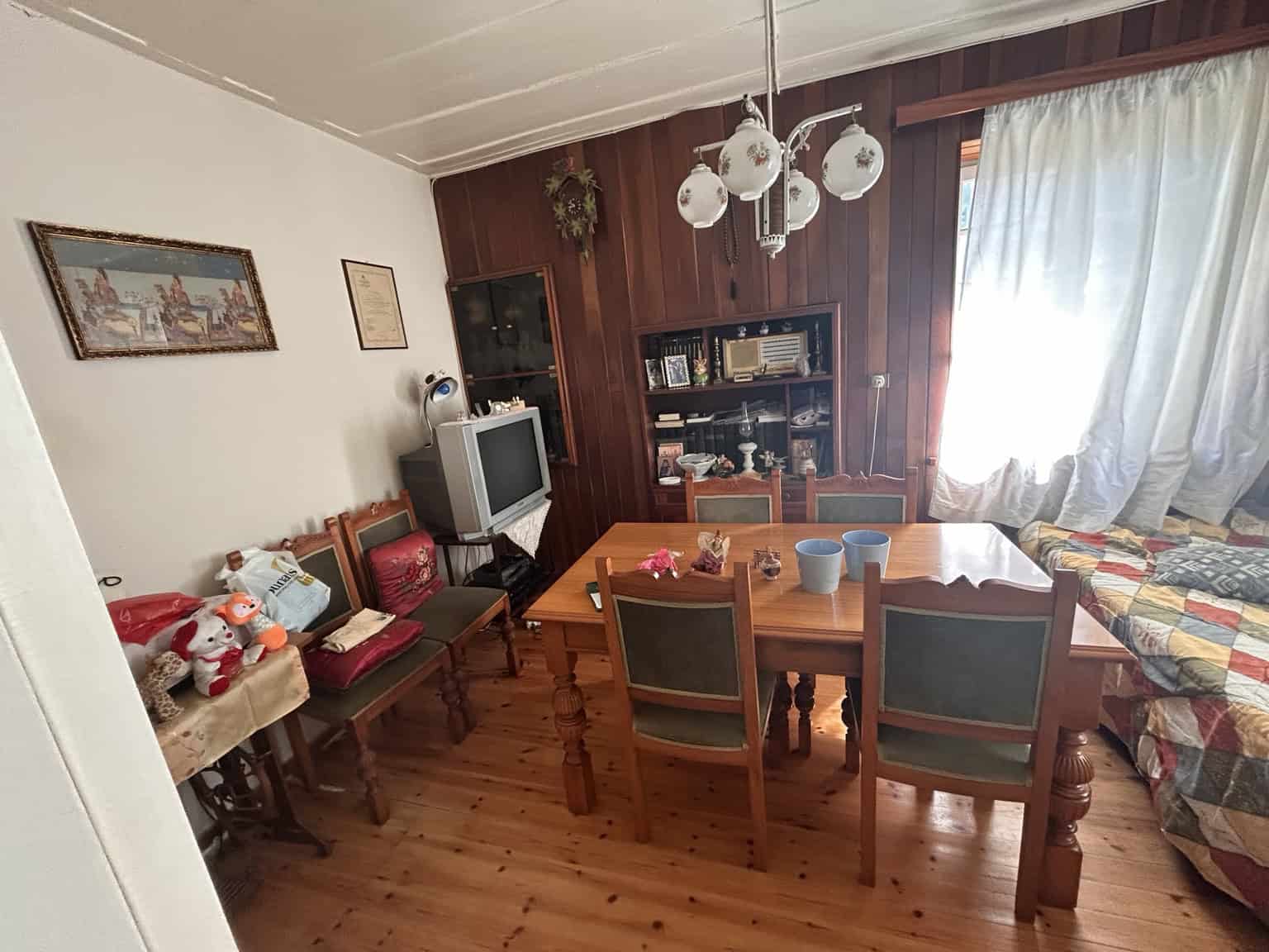 Bright living room with wooden furniture, dining table, and sunlight streaming through curtains.
