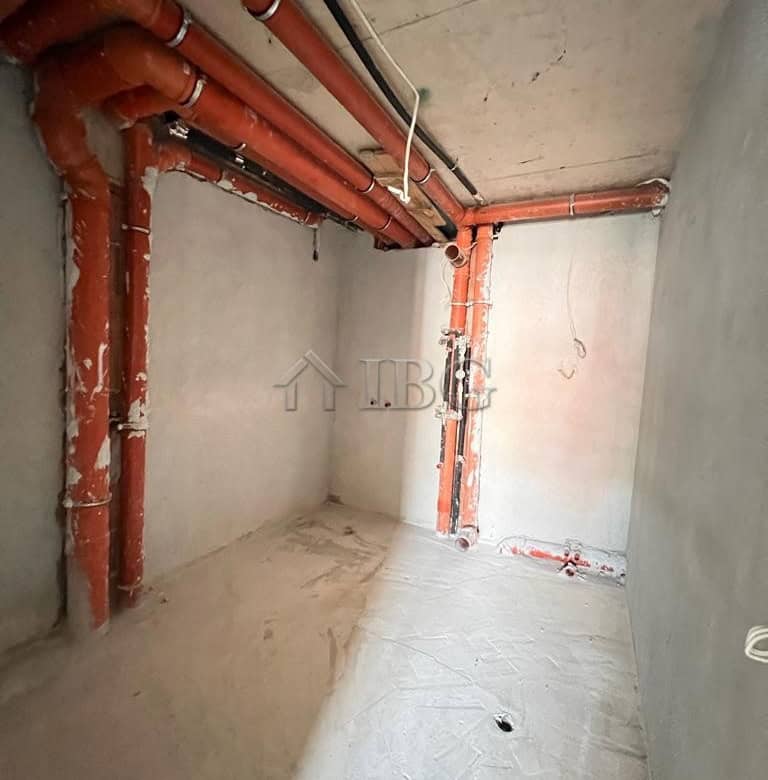 Interior view of an unfinished apartment with exposed plumbing and concrete walls.