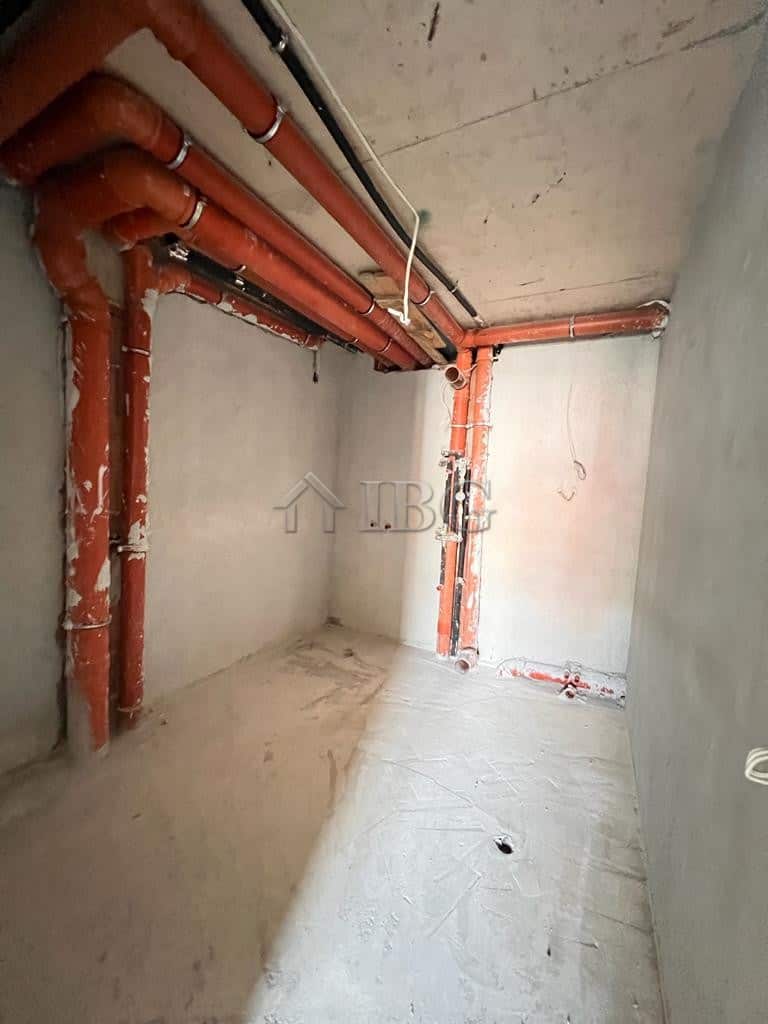 Interior view of an unfinished apartment with exposed plumbing and concrete walls.
