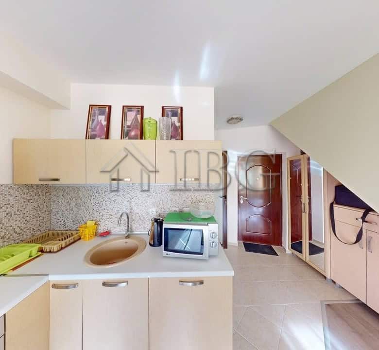 Bright kitchen with beige cabinets, sink, microwave, and green dish rack in Amber Beach apartment.