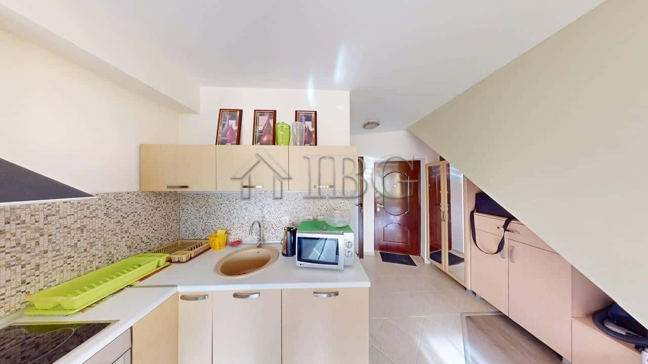 Bright kitchen with beige cabinets, sink, microwave, and green dish rack in Amber Beach apartment.