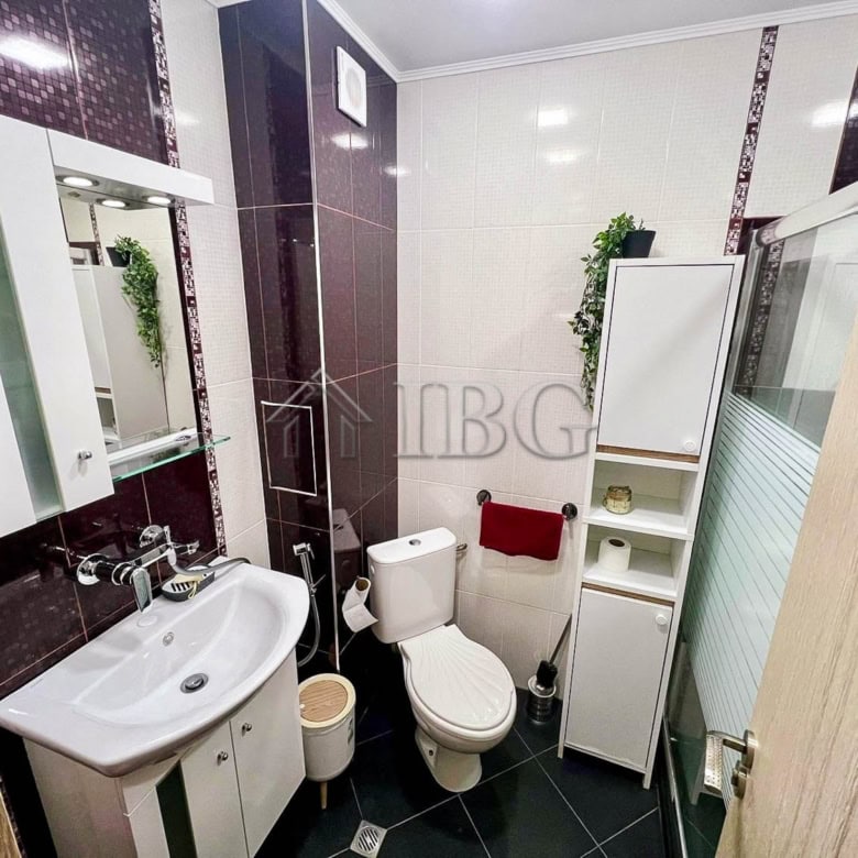 Bright bathroom with white fixtures, dark wall tiles, and green plants in Sarafovo apartment.