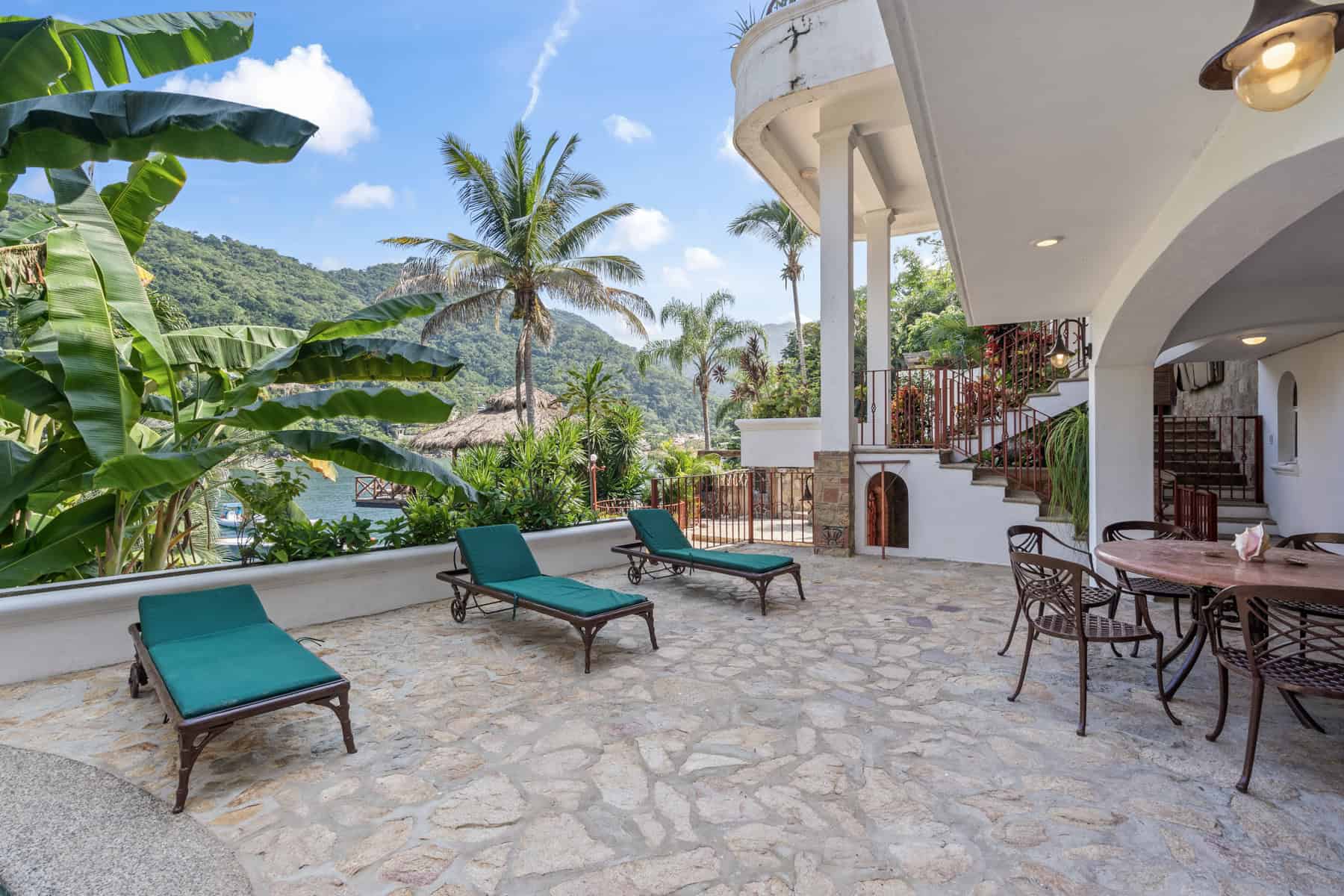 Luxury villa terrace with tropical garden and mountain view, featuring sun loungers and outdoor dini.