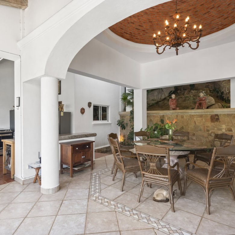 Indoor dining space with tropical plants, chandelier, and rustic furniture.
