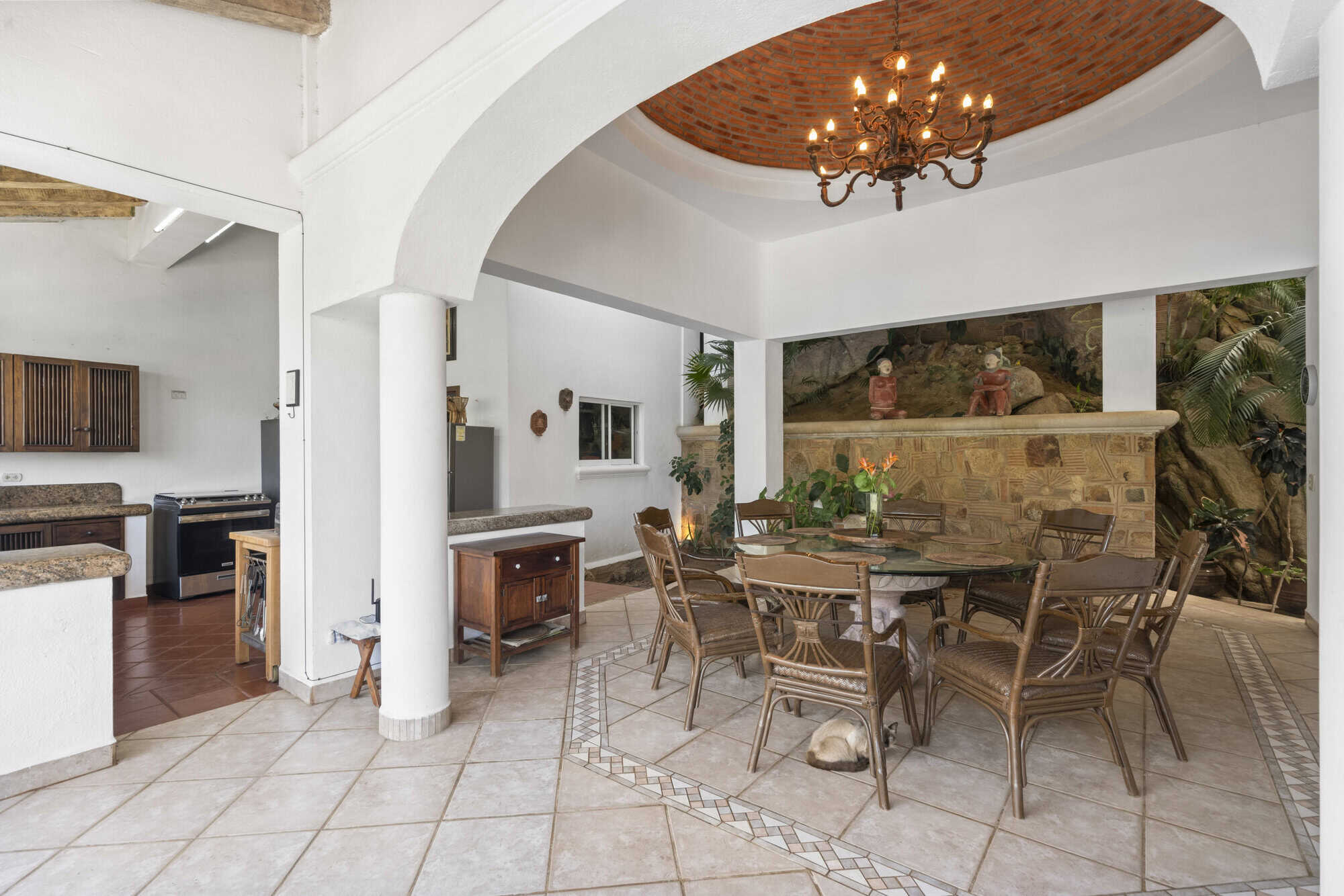 Indoor dining space with tropical plants, chandelier, and rustic furniture.