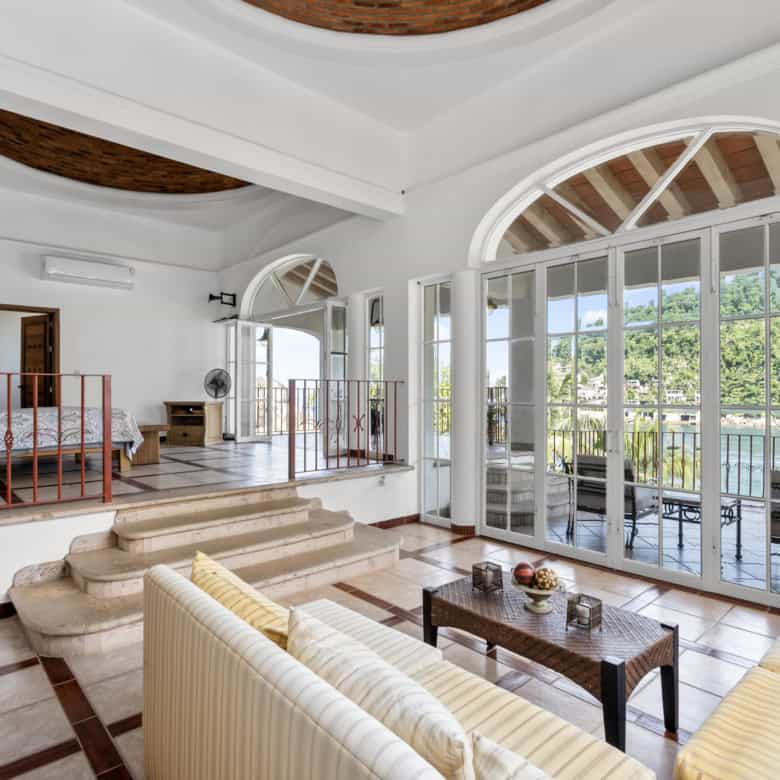 Luxury living room with large glass doors opening to a balcony overlooking lush greenery.