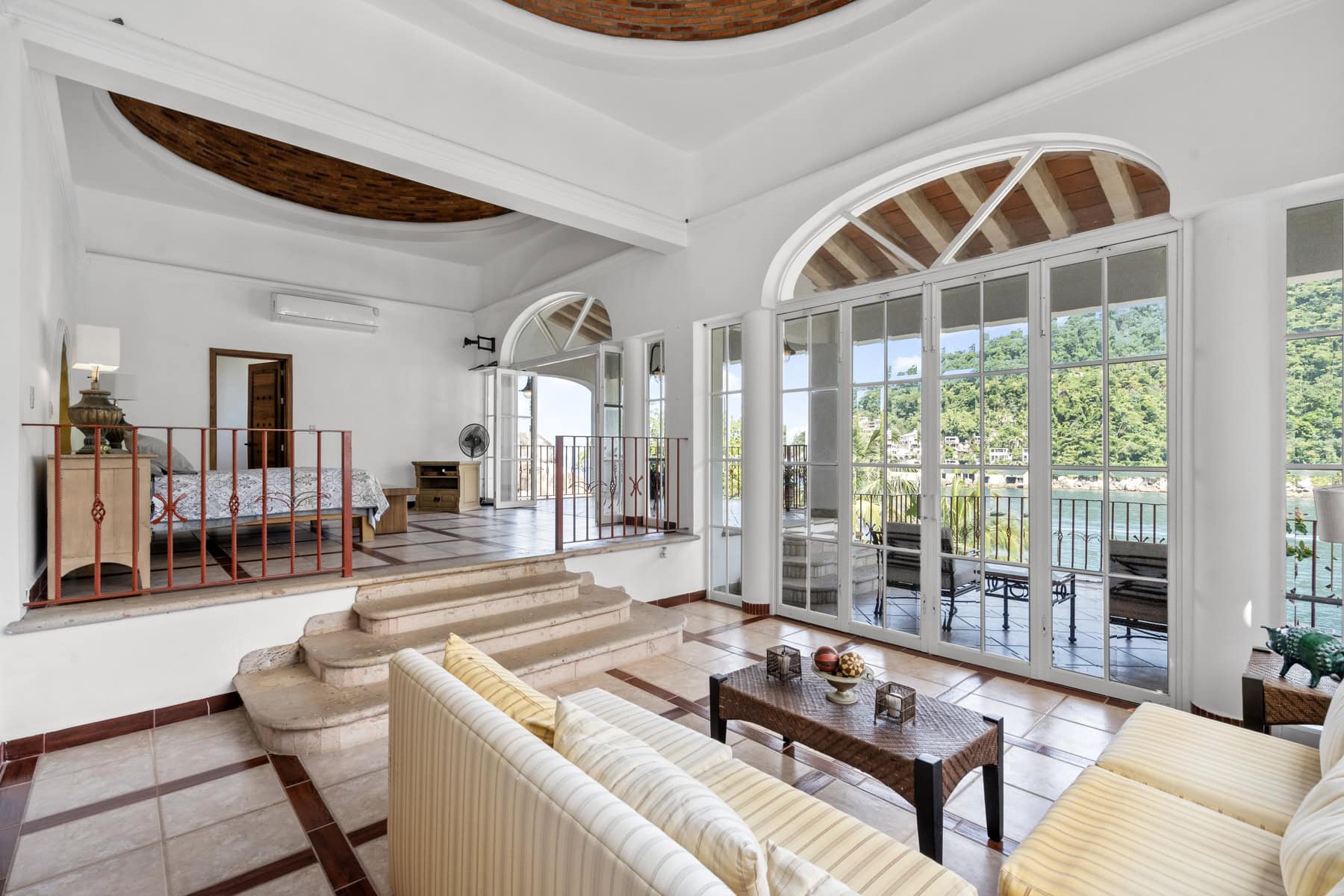 Luxury living room with large glass doors opening to a balcony overlooking lush greenery.