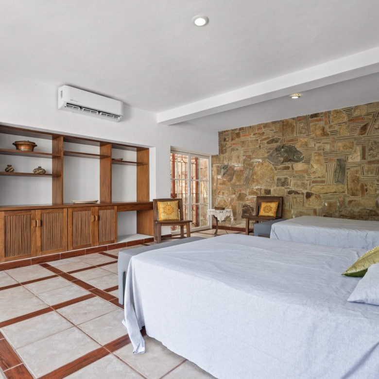 Cozy bedroom featuring a stone accent wall, wooden shelving, and comfortable beds with colorful pill.