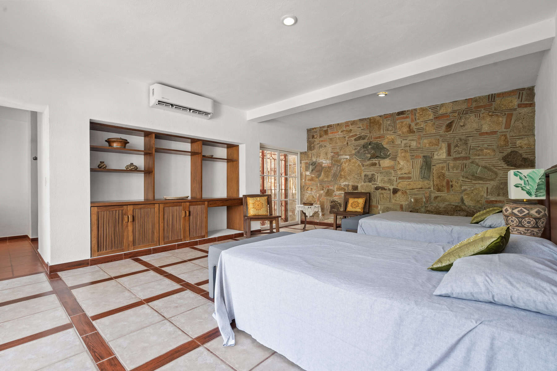 Cozy bedroom featuring a stone accent wall, wooden shelving, and comfortable beds with colorful pill.