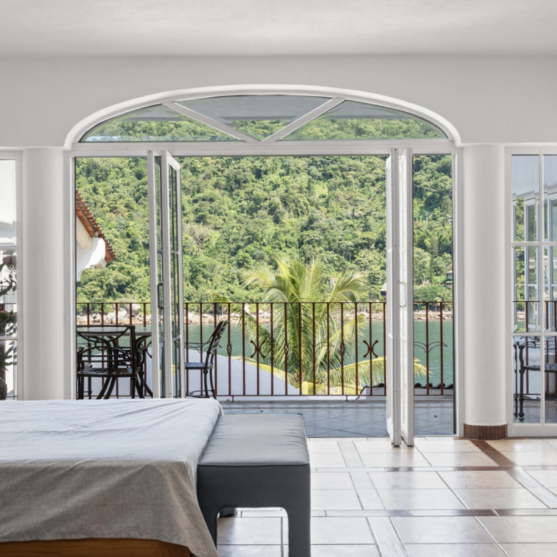 Modern bedroom with balcony overlooking lush greenery and mountains.