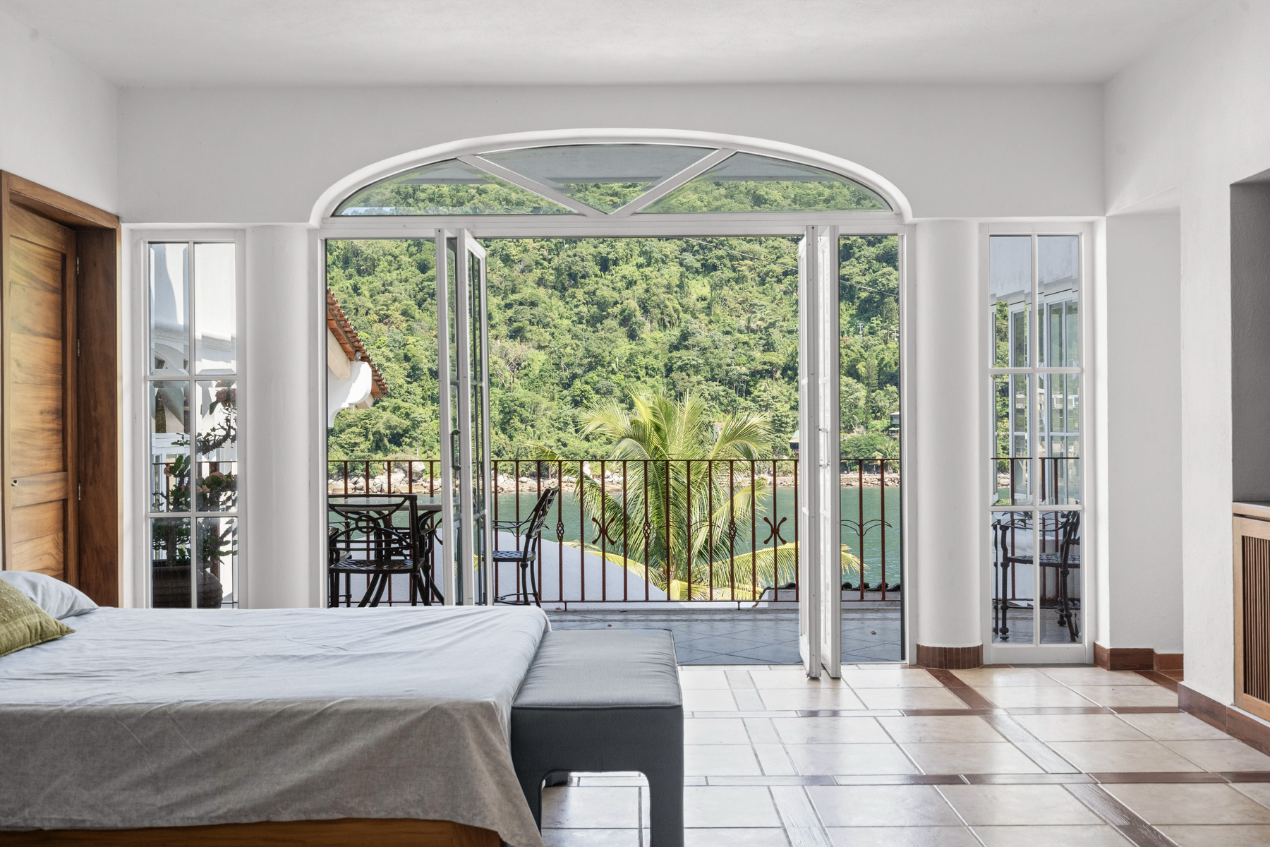 Modern bedroom with balcony overlooking lush greenery and mountains.