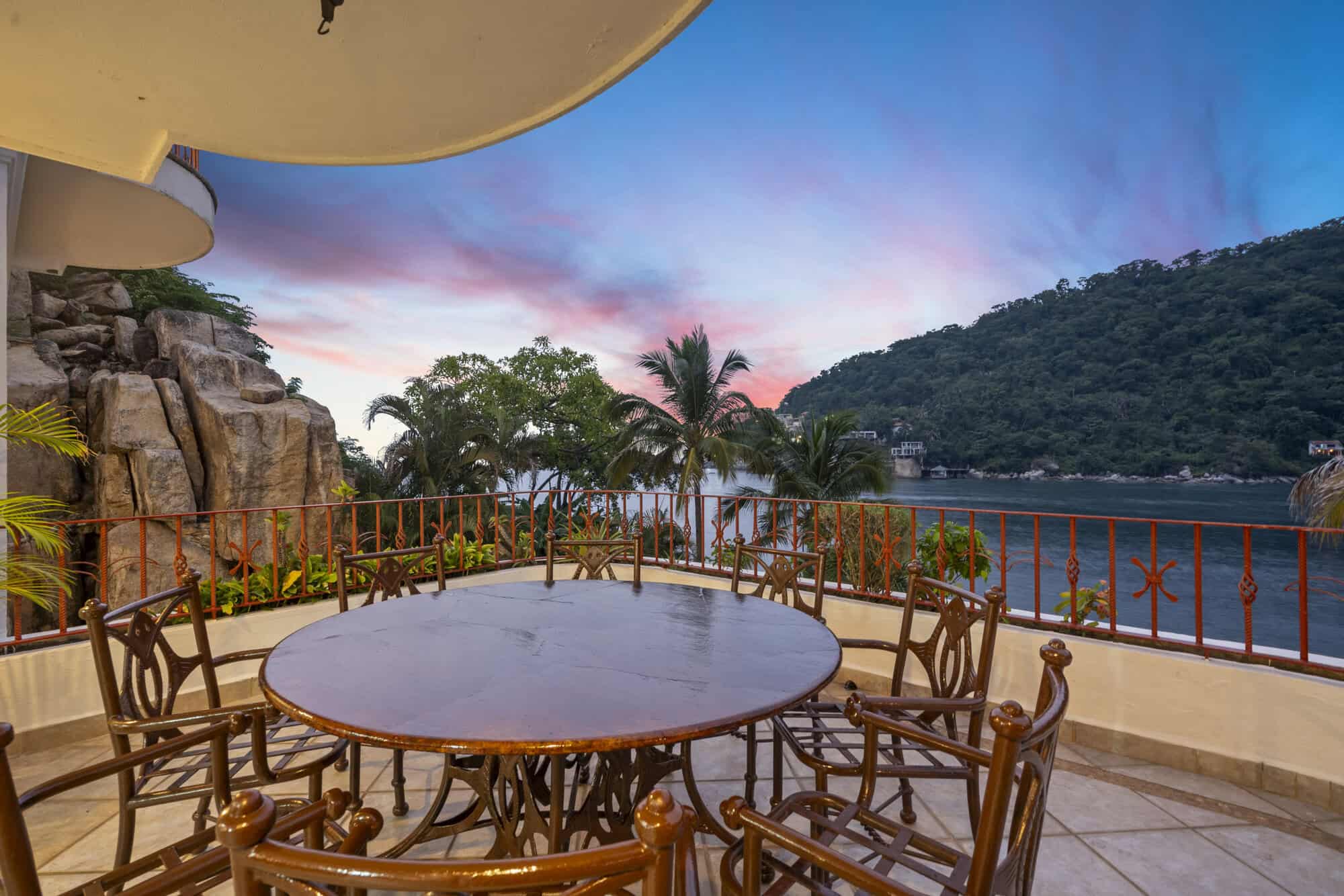 Outdoor dining balcony overlooking the water and lush hills.