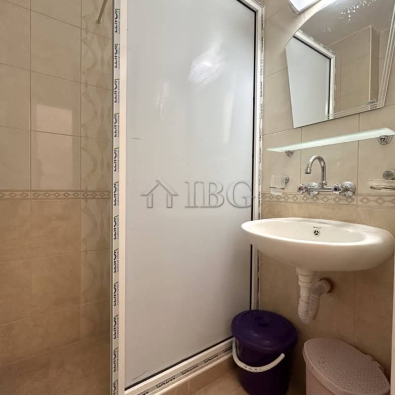 Compact bathroom with shower, sink, and storage in a sunny beach studio.