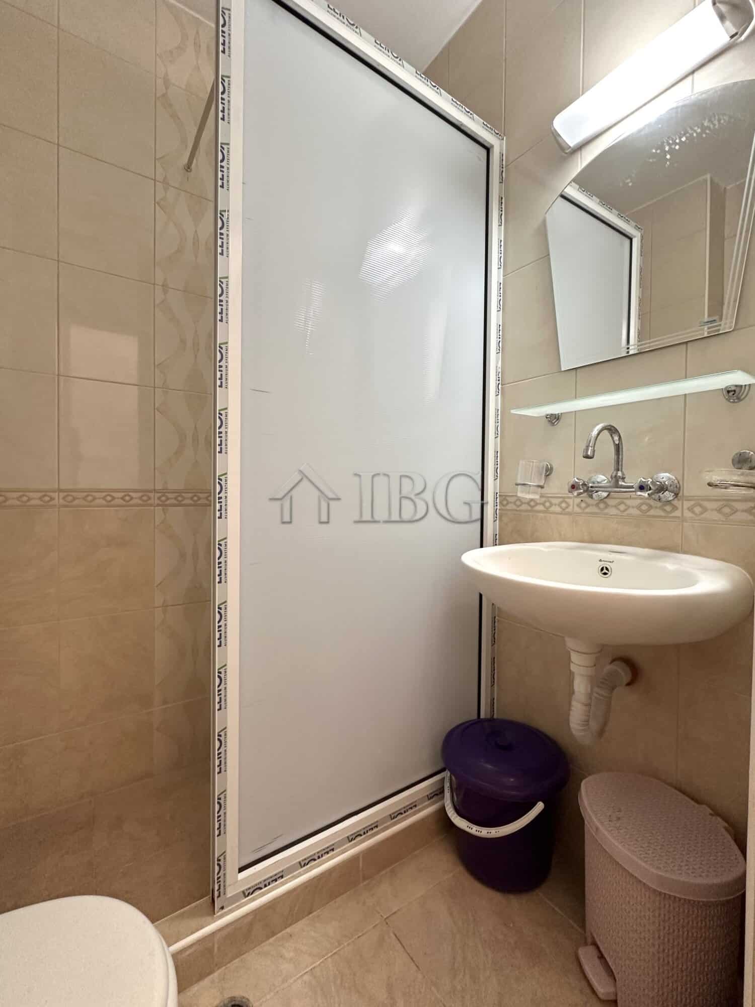 Compact bathroom with shower, sink, and storage in a sunny beach studio.