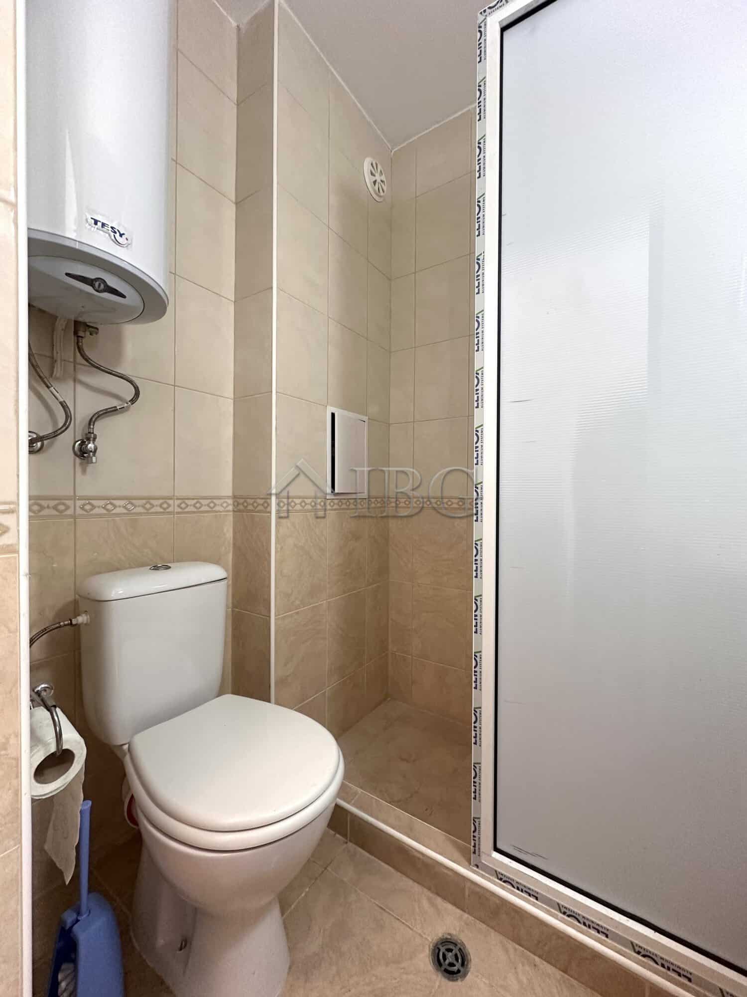 Compact bathroom with shower, toilet, and water heater in a studio apartment.