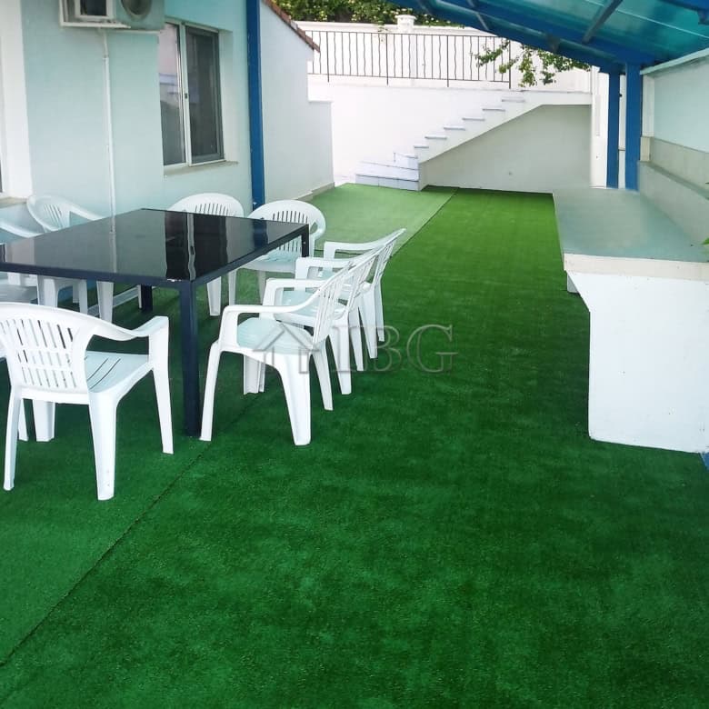 Outdoor terrace of a luxury villa with pool, artificial grass, and seating area under a blue canopy.