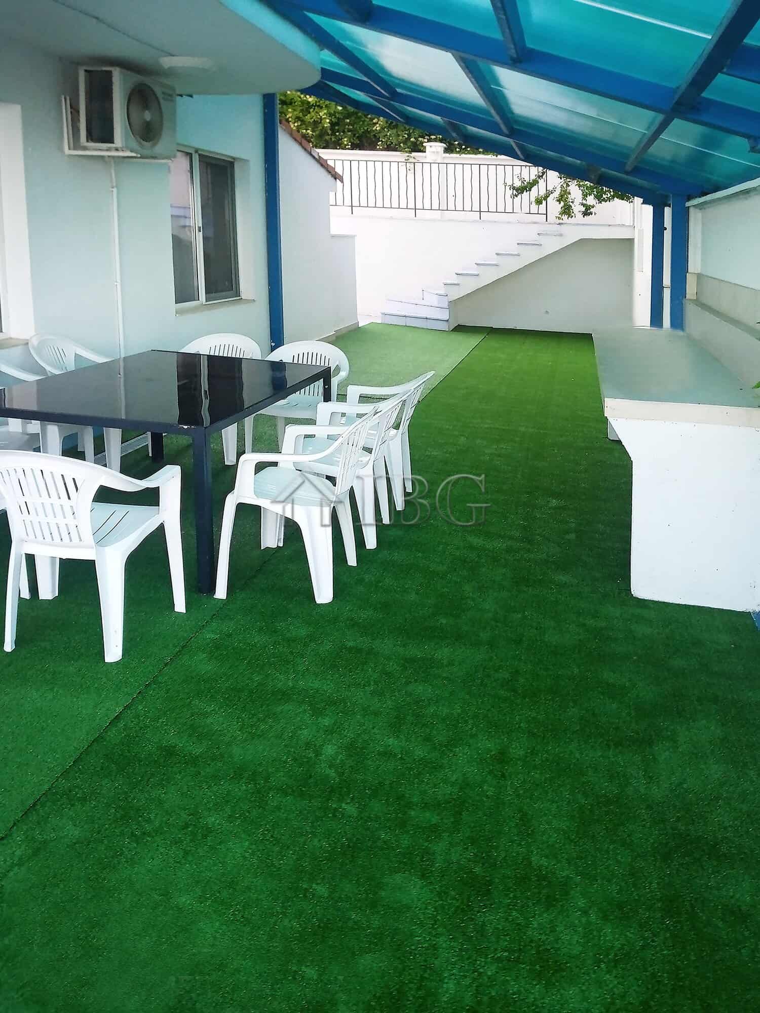 Outdoor terrace of a luxury villa with pool, artificial grass, and seating area under a blue canopy.