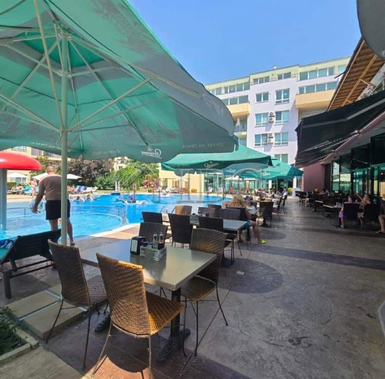 Poolside dining area with tables, chairs, and umbrellas at Pollo Resort, Sunny Beach.