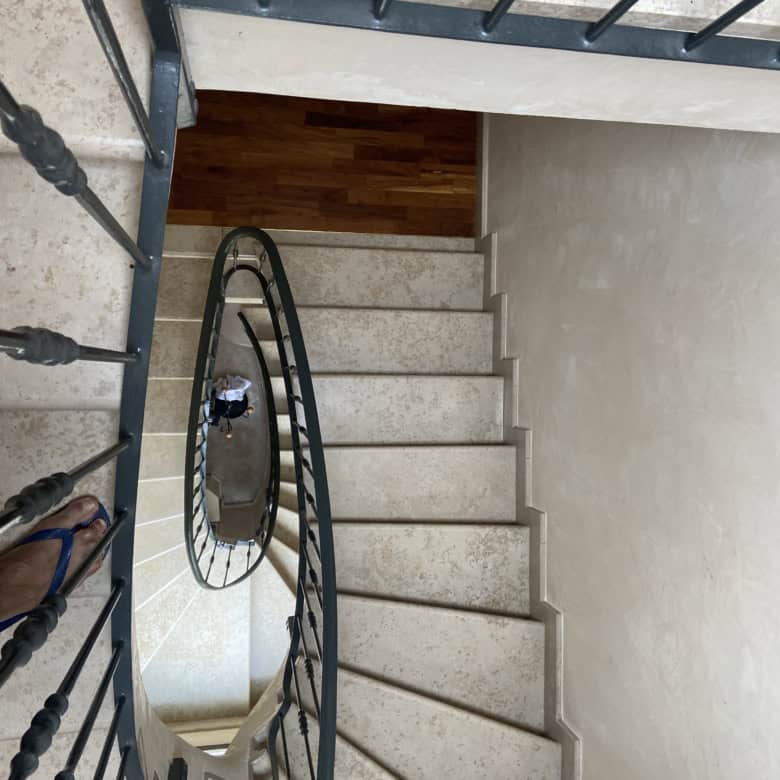 Spiral staircase with black metal railing and beige steps, viewed from above.