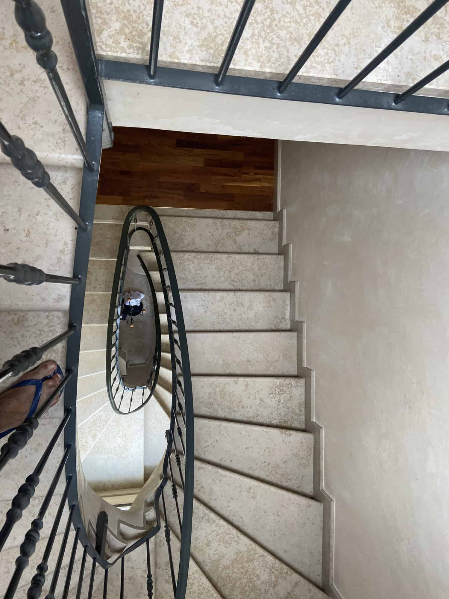 Spiral staircase with black metal railing and beige steps, viewed from above.