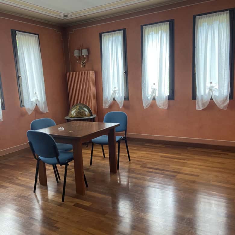 Spacious dining room with wooden floors, four windows with white curtains, and a wooden table with f.