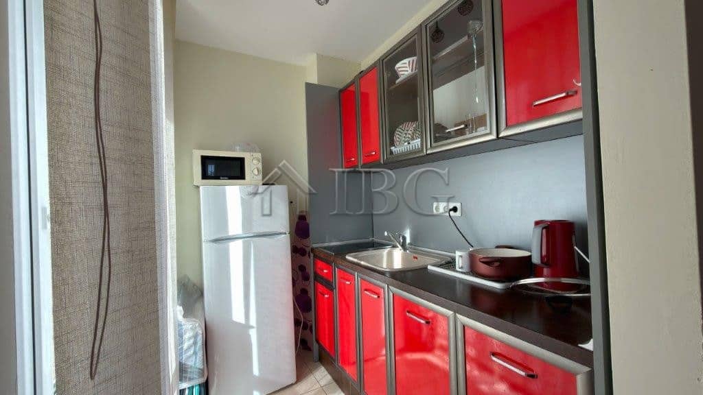Modern studio kitchen with red cabinets and pool view at Orchid Fort Club, Sunny Beach.