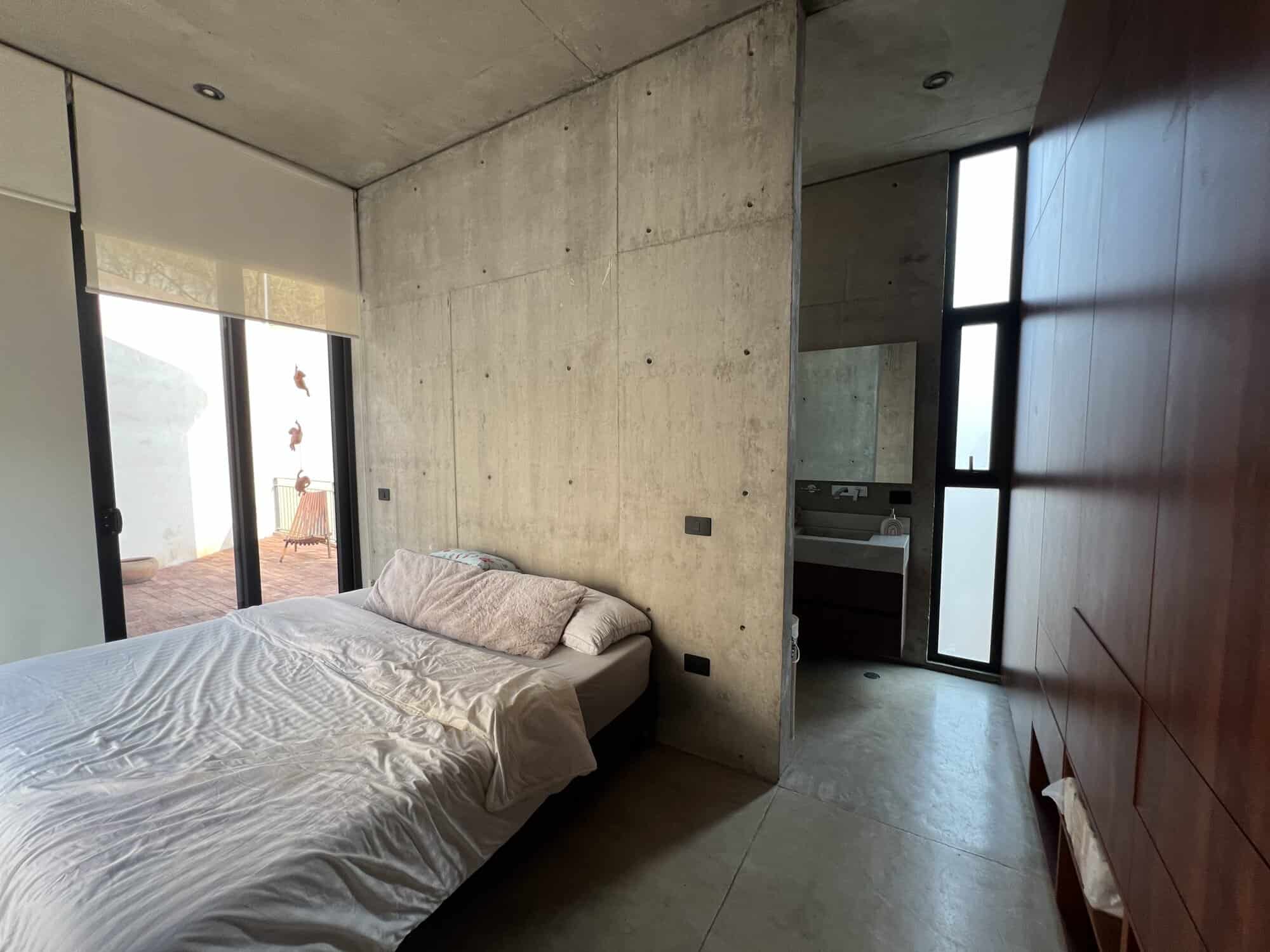 Concrete wall bedroom with large windows and minimalist decor.