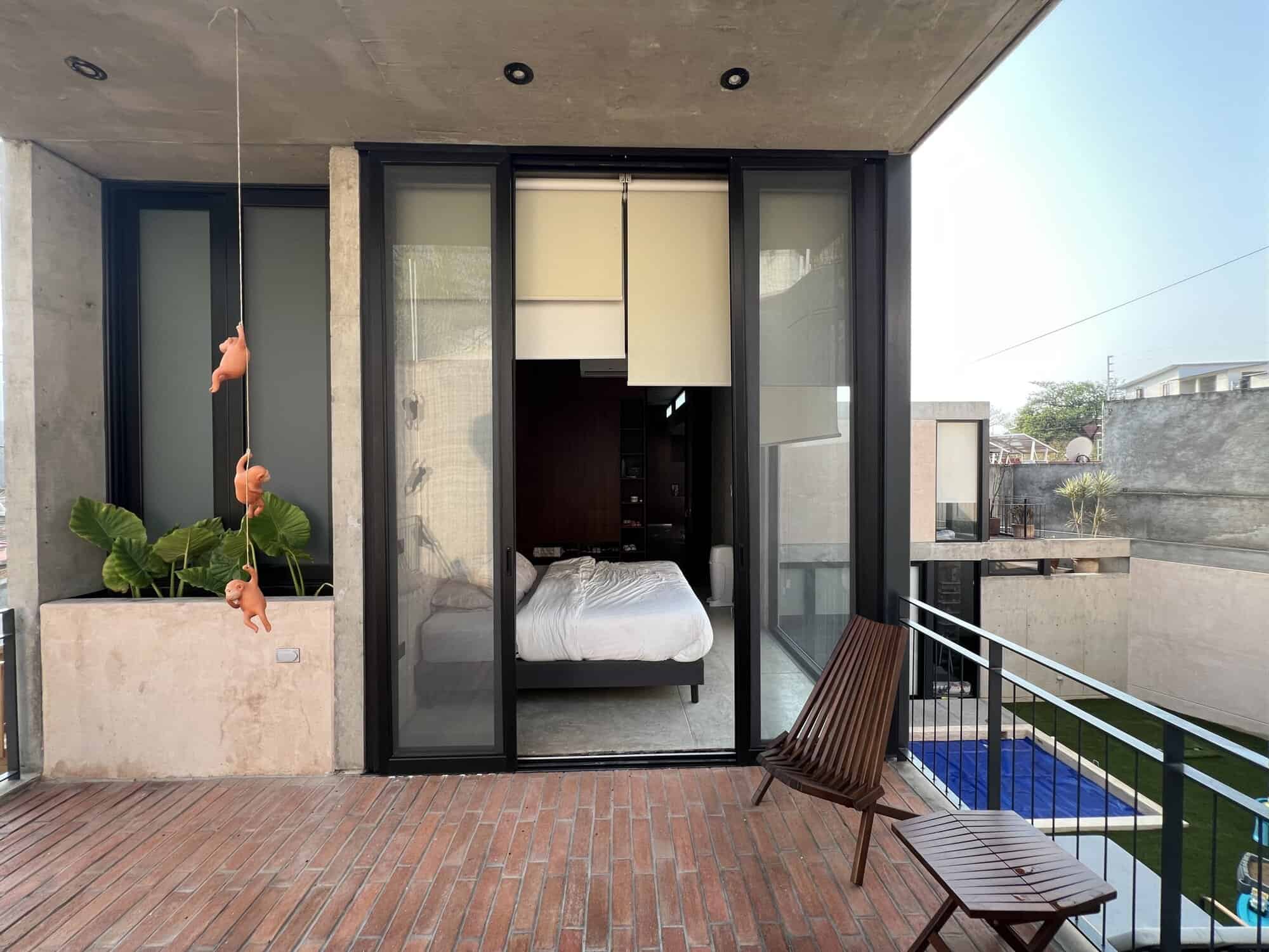Modern bedroom with glass sliding doors opening to balcony and pool area.