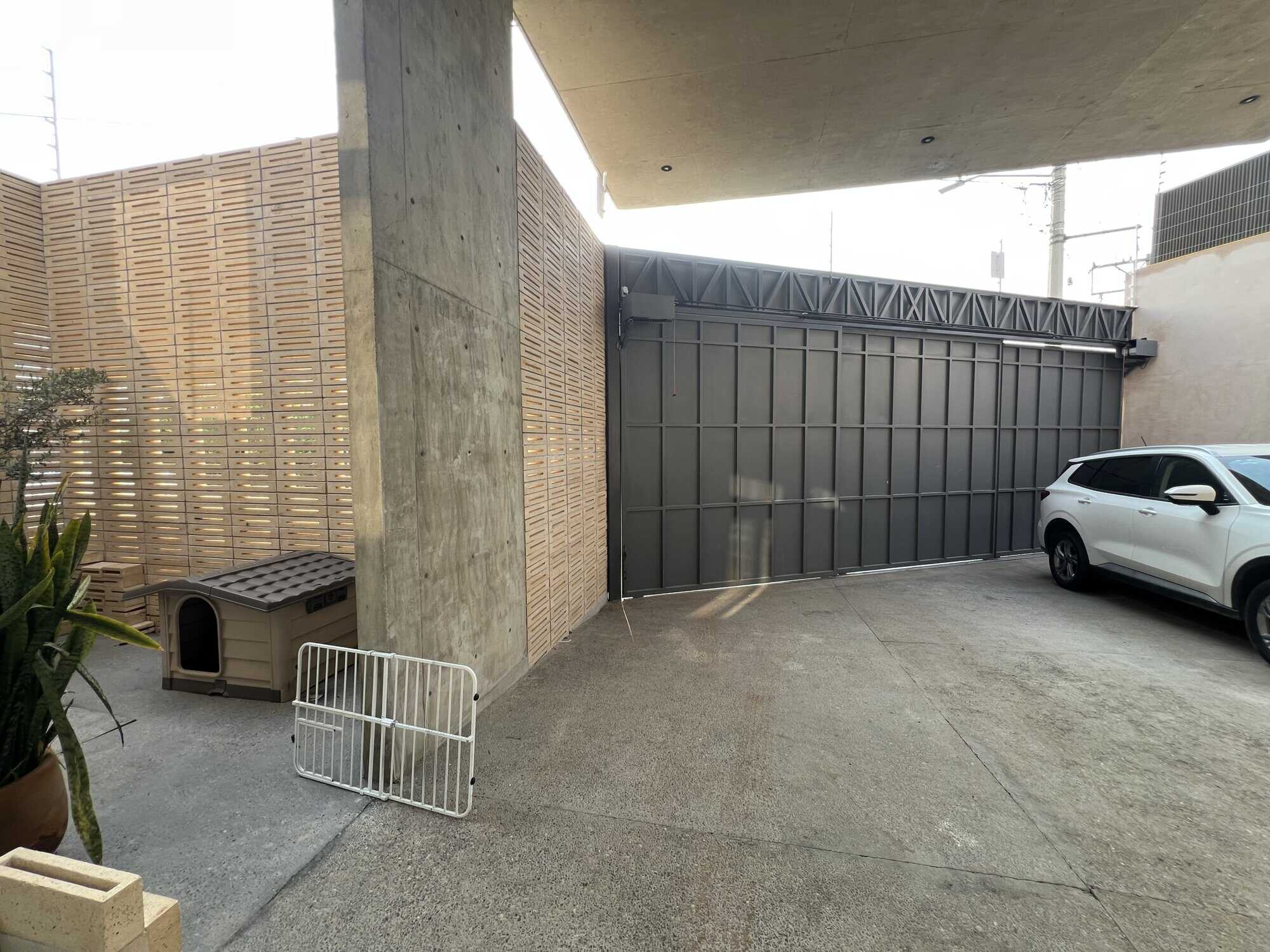 Modern garage with secure black sliding gate and parking area for a vehicle.