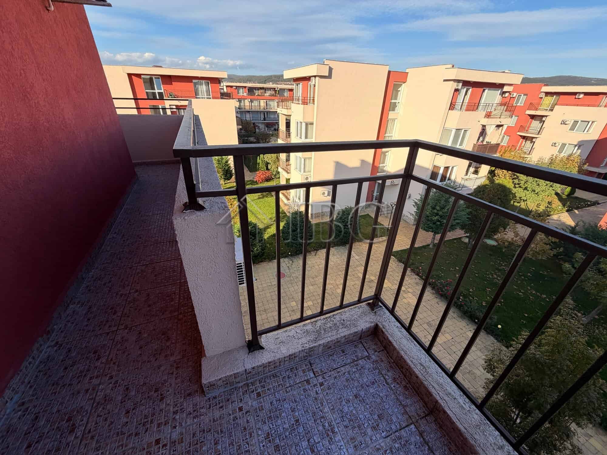 Balcony view of Sunny Beach apartments with colorful buildings and green outdoor space.