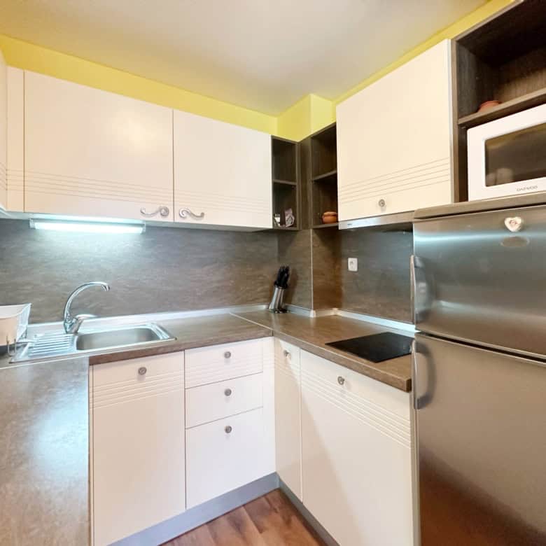 Modern kitchen with white cabinets and stainless steel appliances in Sunny Beach apartment.