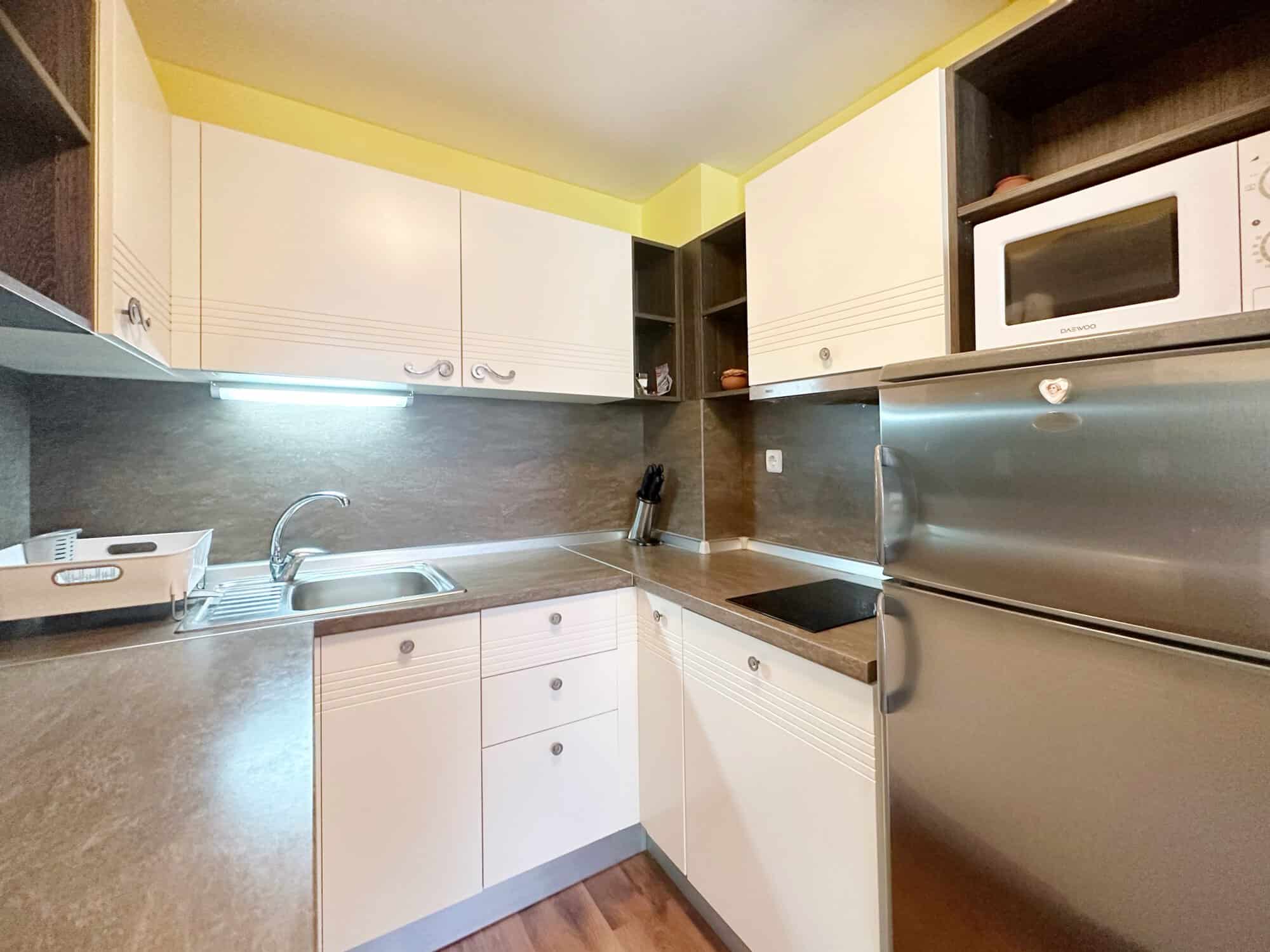 Modern kitchen with white cabinets and stainless steel appliances in Sunny Beach apartment.