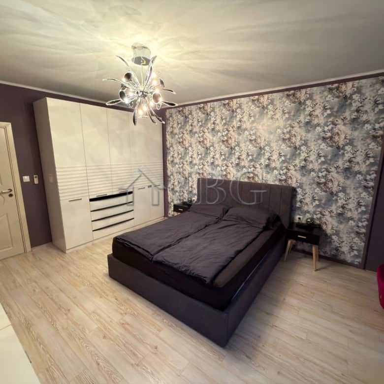 Spacious bedroom featuring a sleek black bed, floral accent wall, and elegant lighting.