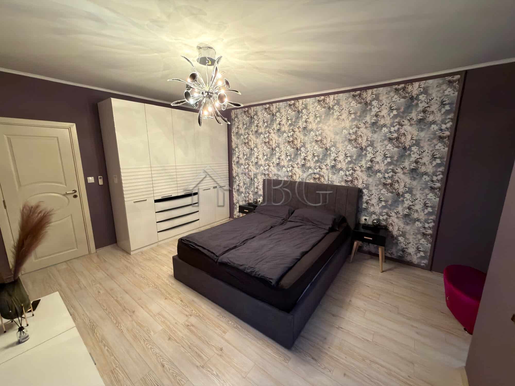 Spacious bedroom featuring a sleek black bed, floral accent wall, and elegant lighting.