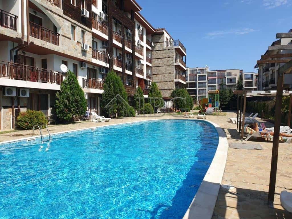 Modern apartment complex with swimming pool in Sveti Vlas. Bright outdoor pool surrounded by residential buildings and sun loungers.