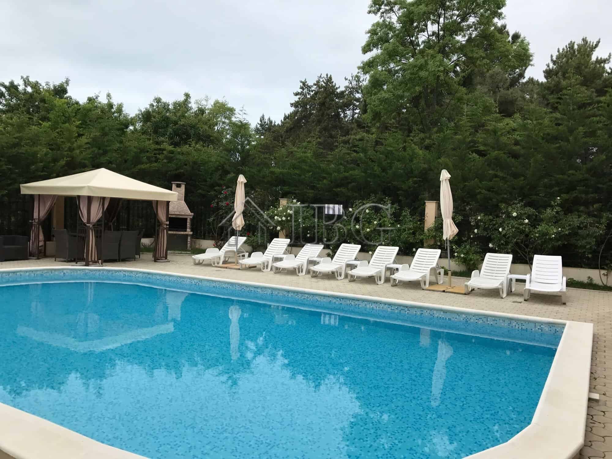 Poolside view of a 1-bedroom apartment with a swimming pool and lush greenery in Pomorie Residence.