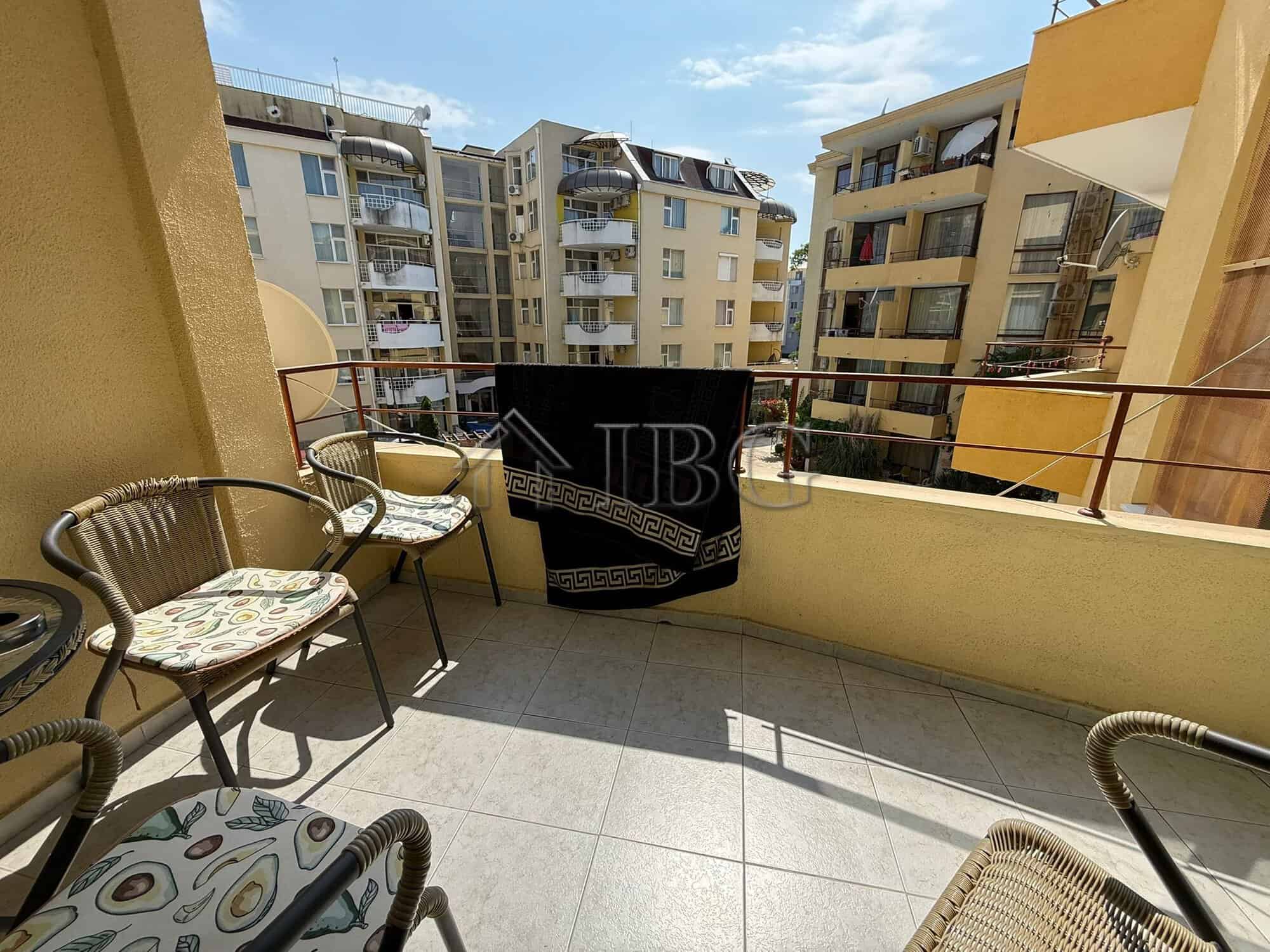 Balcony of a 2-bedroom apartment with seating, overlooking Sunny Beach buildings and blue sky.