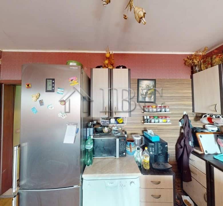 Bright kitchen with refrigerator, microwave, and cooking area in Kosharitsa apartment.