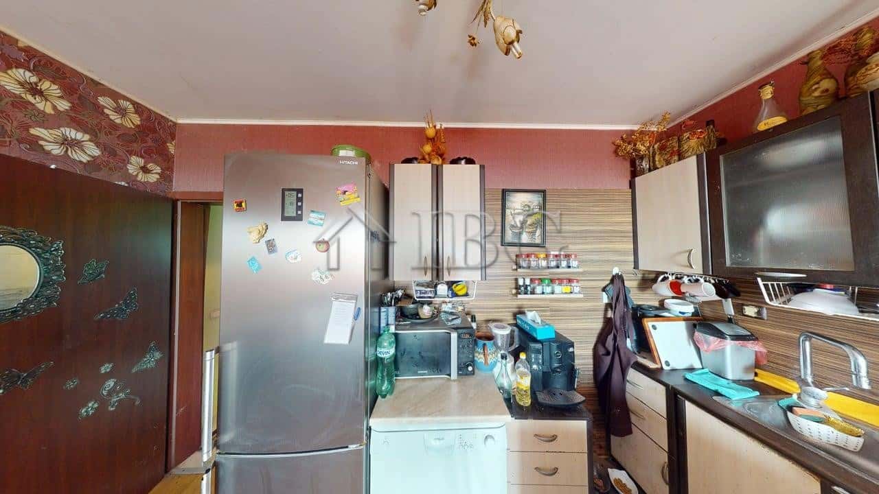 Bright kitchen with refrigerator, microwave, and cooking area in Kosharitsa apartment.