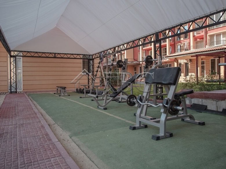 Outdoor gym equipment under a shaded canopy in a residential complex.