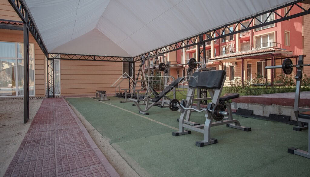 Outdoor gym equipment under a shaded canopy in a residential complex.
