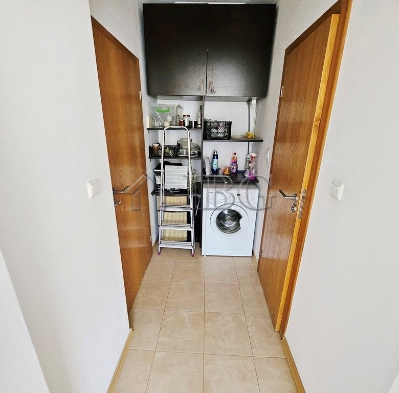 Laundry room with washing machine, storage shelves, and utility space in bright apartment.