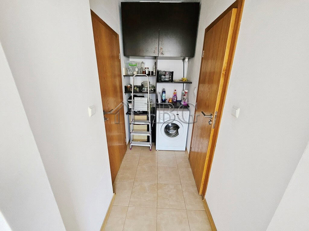 Laundry room with washing machine, storage shelves, and utility space in bright apartment.
