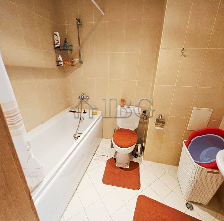 Bright bathroom with bathtub, toilet, and storage shelves in a modern apartment.