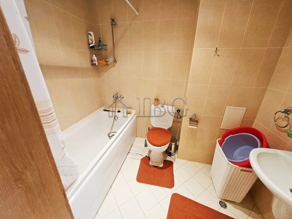 Bright bathroom with bathtub, toilet, and storage shelves in a modern apartment.