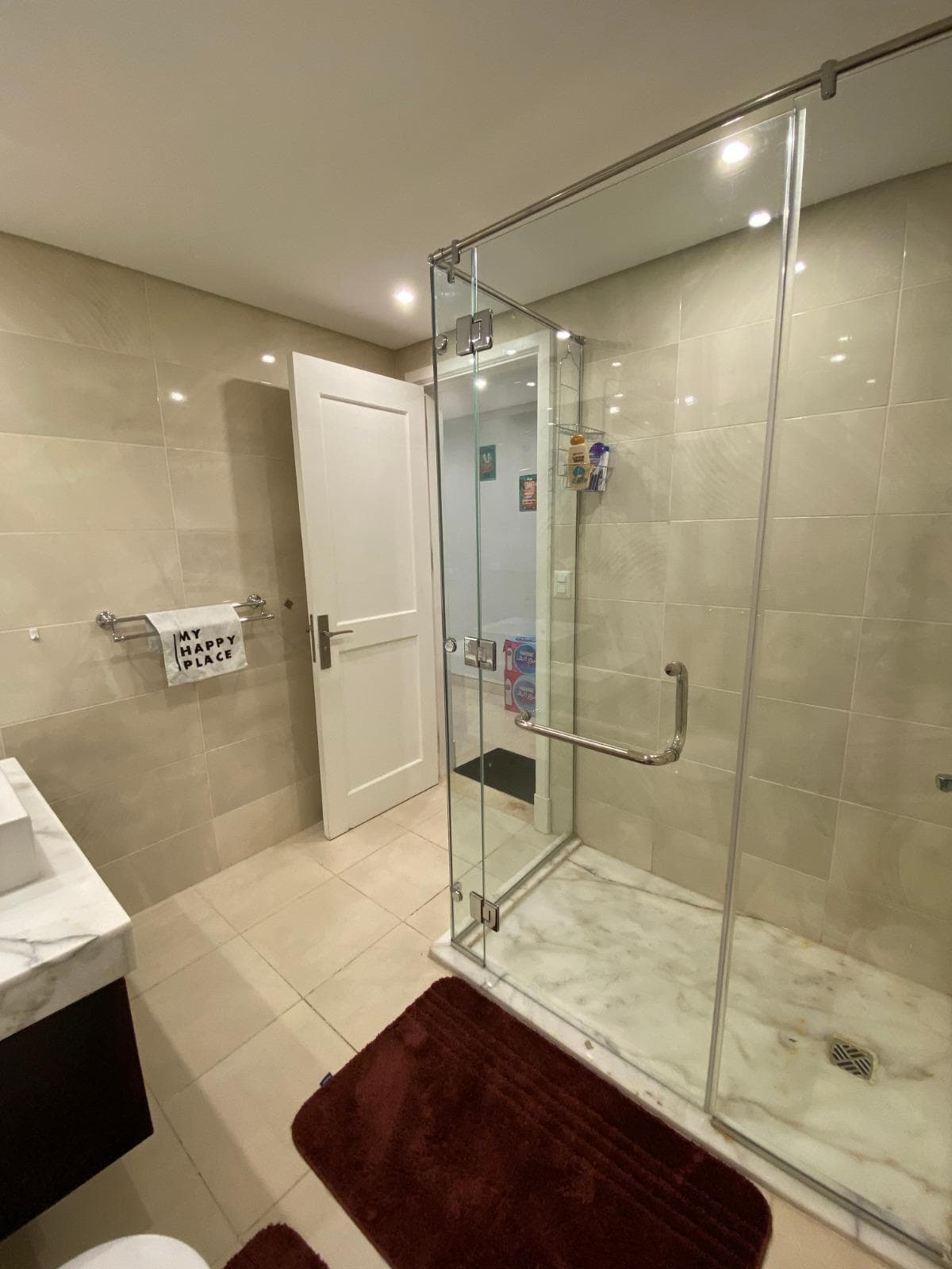 Modern bathroom with glass shower enclosure and beige tiled walls.