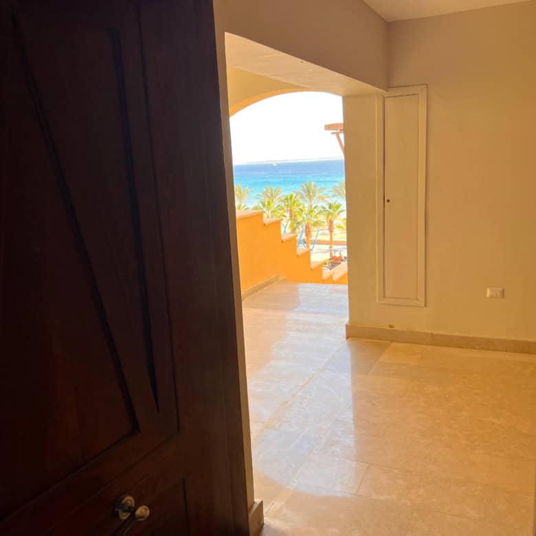 Beach view from a modern apartment doorway, with ocean and palm trees in the background.