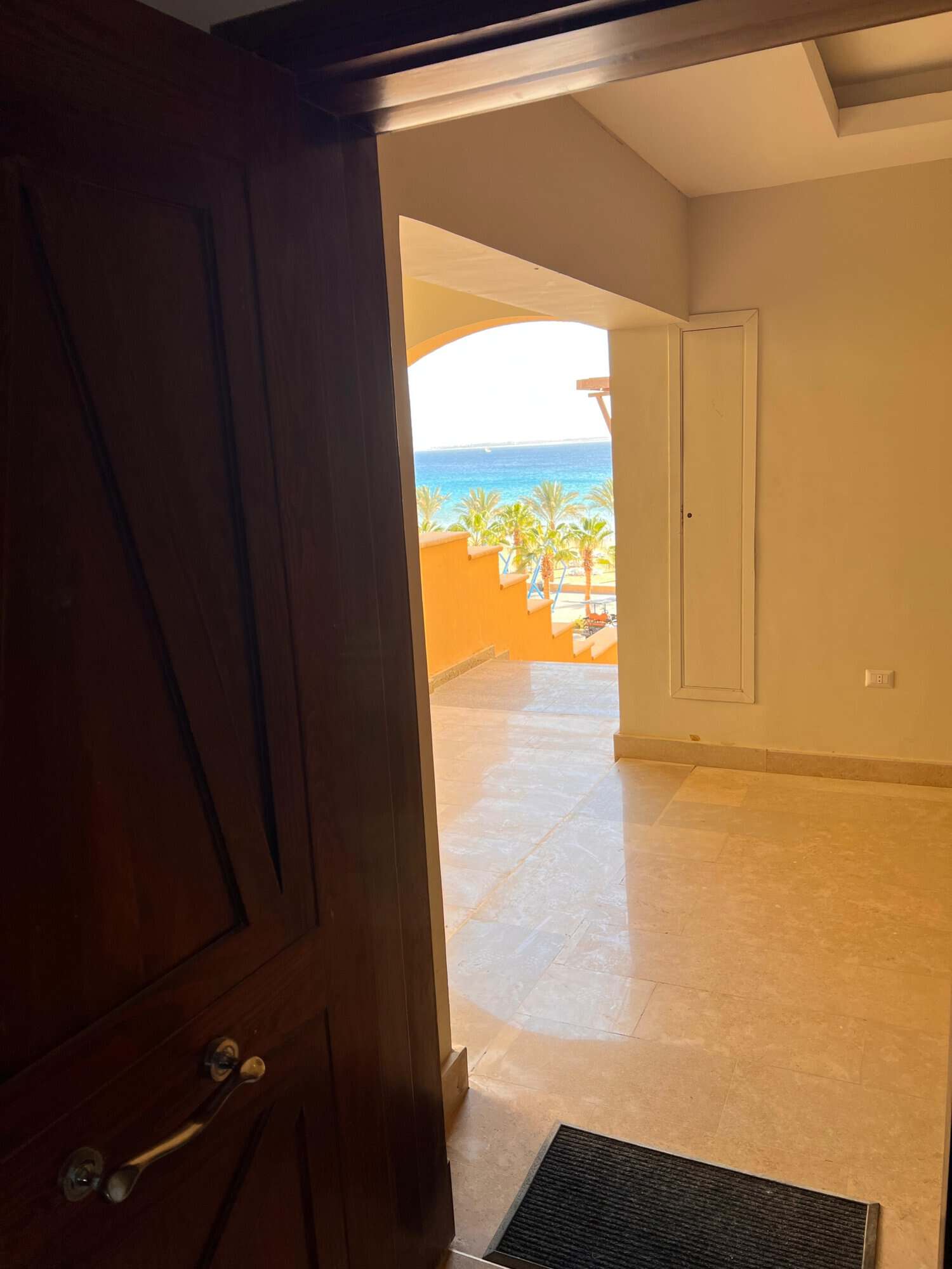 Beach view from a modern apartment doorway, with ocean and palm trees in the background.