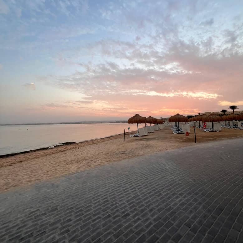 Sunset over a tranquil beach with umbrellas and gentle waves, creating a peaceful seaside scene perf.