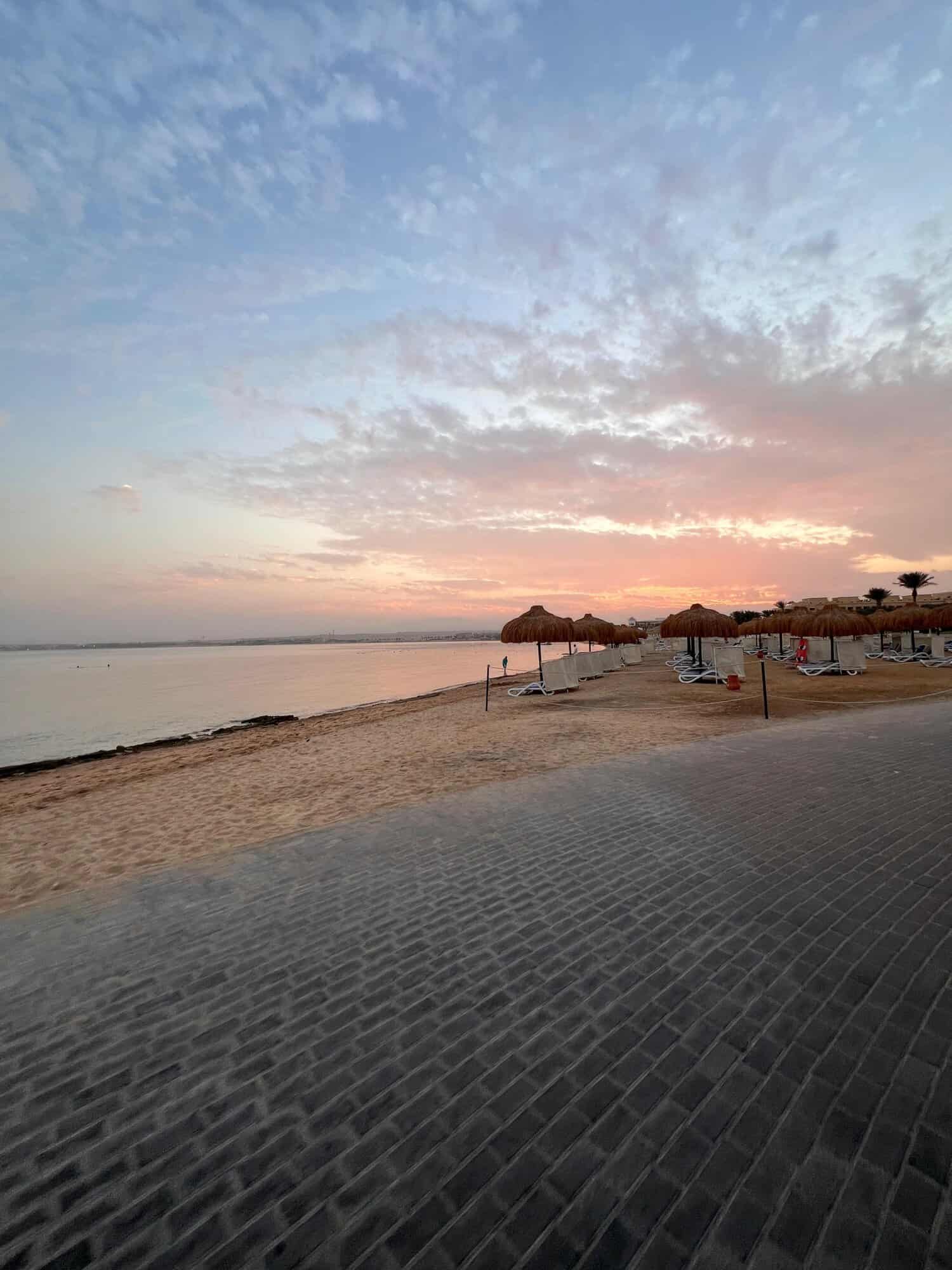 Sunset over a tranquil beach with umbrellas and gentle waves, creating a peaceful seaside scene perf.